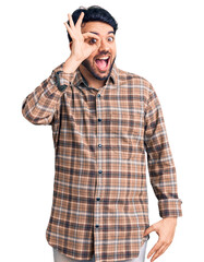 Young hispanic man wearing casual clothes doing ok gesture with hand smiling, eye looking through fingers with happy face.