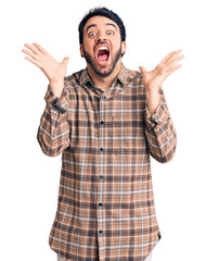 Young hispanic man wearing casual clothes celebrating mad and crazy for success with arms raised...