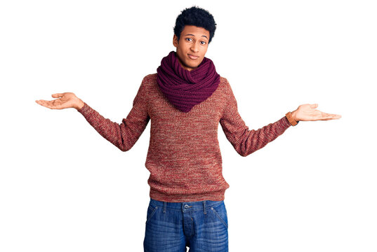Young african american man wearing casual winter sweater and scarf clueless and confused expression with arms and hands raised. doubt concept.
