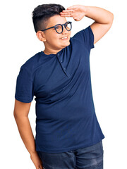 Fototapeta premium Little boy kid wearing casual clothes and glasses very happy and smiling looking far away with hand over head. searching concept.