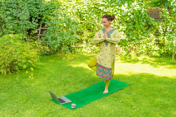 woman doing yoga in nature online using laptop - 780968068