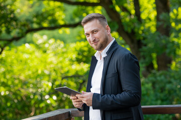 friendly businessman with a tablet against a background of green trees - 780968222