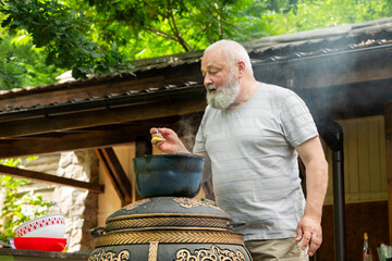 an elderly man prepares pilaf in the yard - 780968256