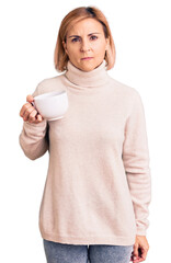 Young blonde woman holding coffee thinking attitude and sober expression looking self confident