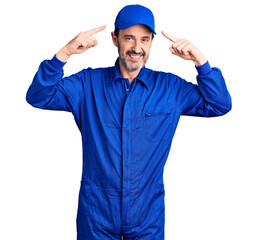 Middle age handsome man wearing mechanic uniform smiling pointing to head with both hands finger, great idea or thought, good memory