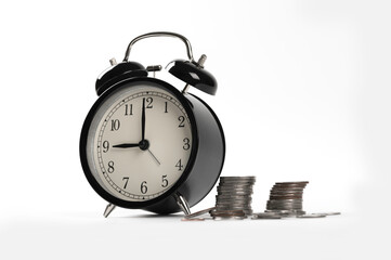 Black alarm clock with stack of coin on white background.