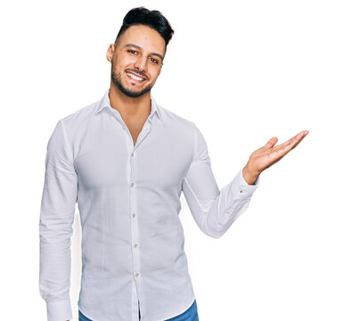 Young arab man wearing casual clothes smiling cheerful presenting and pointing with palm of hand looking at the camera.