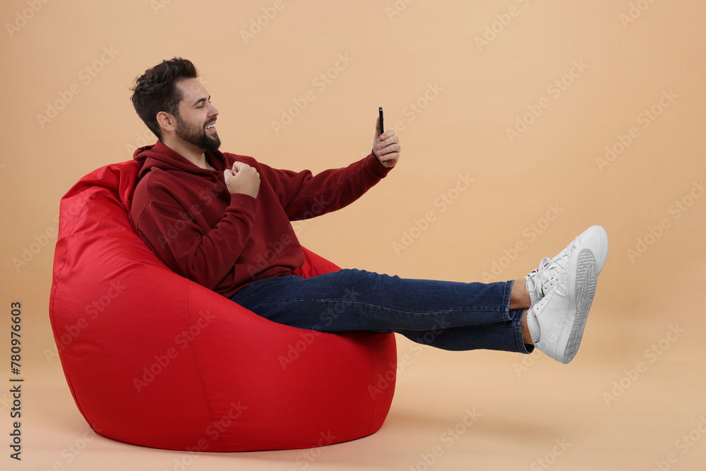 Poster happy young man using smartphone on bean bag chair against beige background