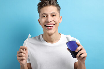 Young man with mouthwash and toothbrush on light blue background