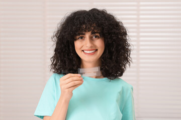Young woman holding teeth whitening strips indoors