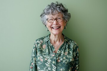 Portrait of a smiling senior woman wearing glasses against a green wall