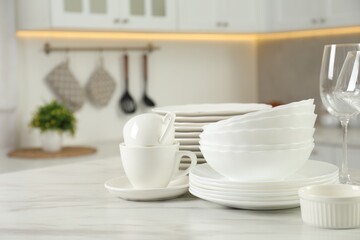 Clean plates, bowls, cups and glasses on white marble table in kitchen