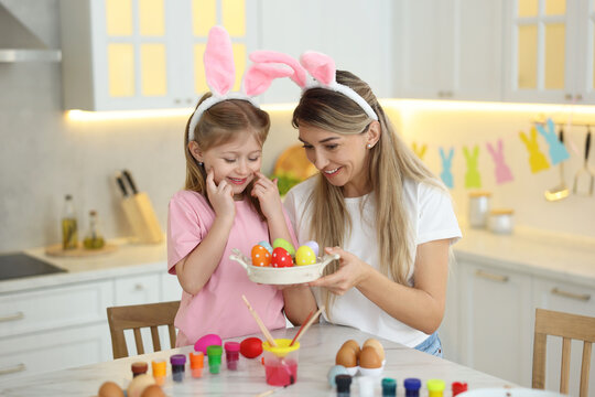 Easter celebration. Happy mother and her cute daughter with painted eggs at white marble table in kitchen