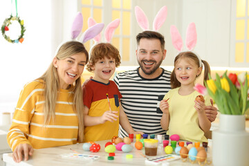 Painting Easter eggs. Happy family with bunny ears at white marble table in kitchen