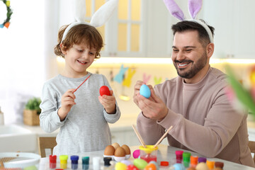 Easter celebration. Happy father with his little son painting eggs at table in kitchen