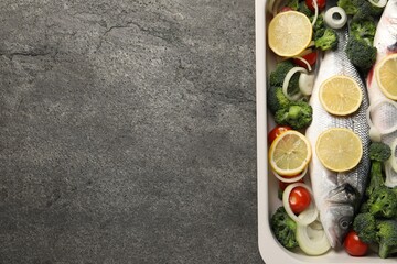 Raw fish with vegetables and lemon in baking dish on grey textured table, top view. Space for text