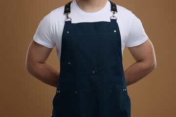 Man in kitchen apron on brown background, closeup. Mockup for design