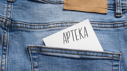 White card with a handwritten inscription "Apteka", inserted into the pocket of blue pants jeasnow (selective focus), translation: Pharmacy