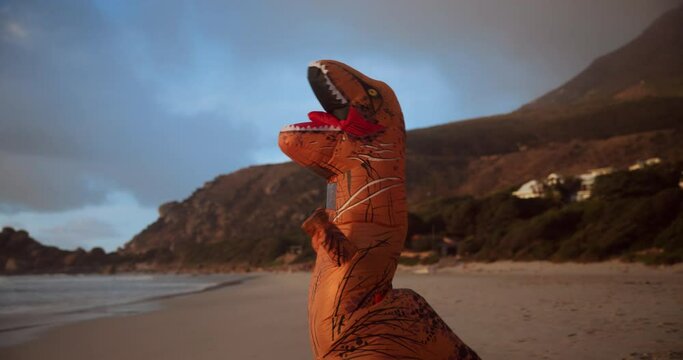Beach, inflatable and dinosaur costume or comic, celebration and ocean at sunrise. Summer, funny or comedy for weird prehistoric doll or toy, sea or sand at dawn outside for humour on Hawaii seaside