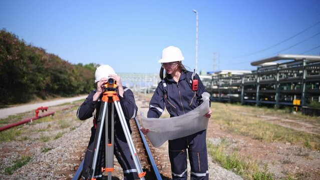 Surveyor engineers team wearing safety uniform and blueprint checking inspection by theodolite telescope to measurement level position railway construction site is industry transportation concept.