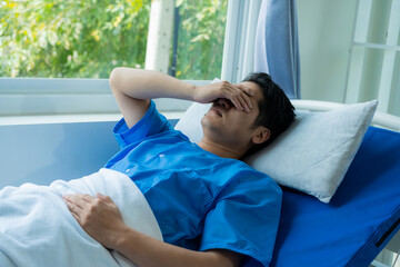 A young Asian patient had a headache in a hospital bed while wearing a blue uniform while being...