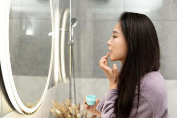 Woman Applying Lip Balm In Bathroom Mirror Reflection Self-Care Routine Hygiene Concept