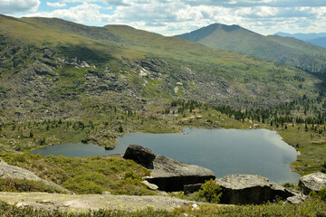A view from the top of a rocky mountain to a large beautiful lake surrounded by mountain ranges on a summer morning.