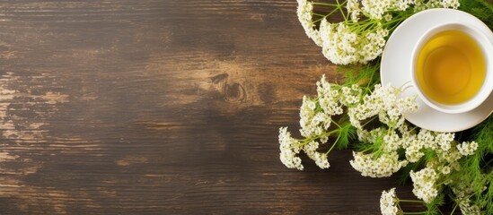 Close-up of a herbal tea cup decorated with fresh yarrow flowers placed on a wooden table - obrazy, fototapety, plakaty