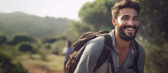 A content man with a backpack is smiling as he walks along a countryside hiking trail in an open field - obrazy, fototapety, plakaty