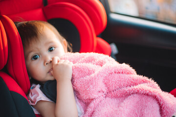 Asian Toddler Girl seats peacefully in her red carseat. She is holding her pink blanket while...