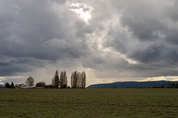 Dramatic sky with early spring storm clouds and rain just before sunset, above and empty farm...