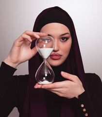 Beautiful arab businesswoman wearing hijab and holding sand clock. Time is passing and it's a pressure concept. - 781033069