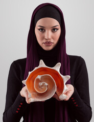 Pretty stylish Muslim woman wearing hijab and holding a seashell and dreams closed eyes. Golden ratio and ideal proportion concept. - 781036263