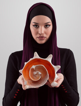 Pretty stylish Muslim woman wearing hijab and holding a seashell and dreams closed eyes. Golden ratio and ideal proportion concept.