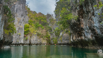 Canoes with tourists sail along a calm emerald lagoon surrounded by karst rocks. Green tropical...