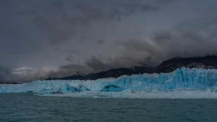 A wall of blue ice stretches over a glacial lake. Melted ice floes, broken off icebergs float in...
