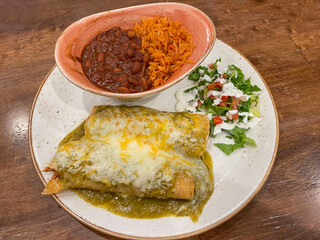 A plate with two chicken enchilada with green sauce, rice and beans and a small salad on the side.