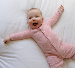 Beautiful smiling baby girl on a white bed in a pink onesie