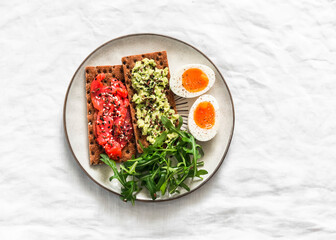Rye crackers with avocado and salmon, boiled egg, arugula - delicious breakfast, snack on a light background, top view