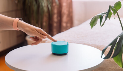 A woman's hand touches her finger to a blue smart speaker on the table.