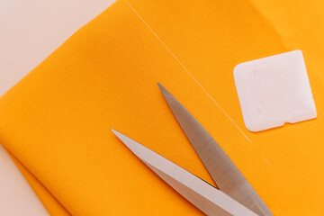 Sewing scissors and chalk close-up lie on orange fabric.