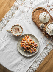 Coffee break - cappuccino and waffles with condensed milk on a round wooden table