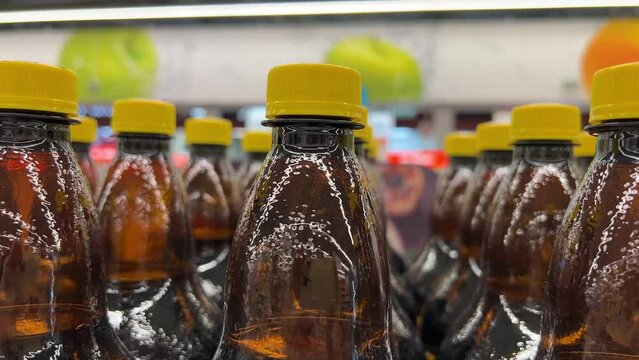 Many brown plastic bottles of drinks with yellow caps on store shelf in supermarket, warehouse