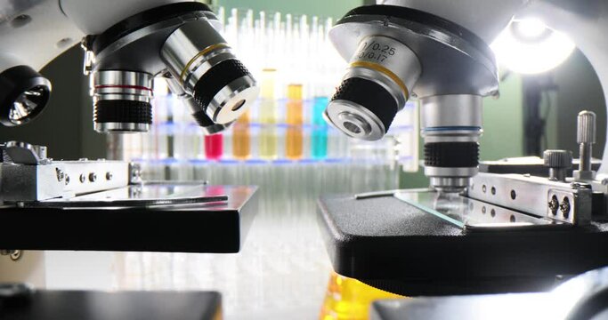 Many microscopes and test tubes with colored liquids on a table in a chemical laboratory