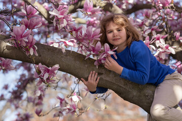 Happy spring. Kid climbing magnolia tree. Close up portrait of smiling child face near blossom...