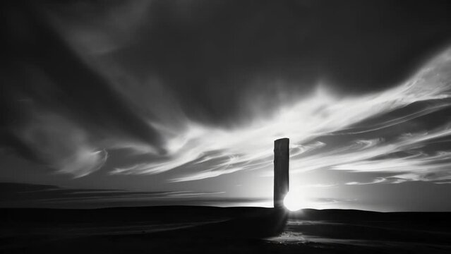 A monochromatic photograph captures the beauty of a lone monolith against the backdrop of a fiery sunrise a reminder of the coexistence of urban and natural environments.