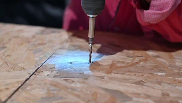 Close-up image of a craftsperson's hands drilling a hole in a plywood surface