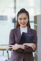 Asian businesswoman stands in an office with a tablet in her hands.