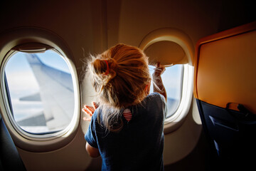 Adorable little girl traveling by an airplane. Child sitting by aircraft window and looking...