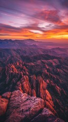 A panoramic view of a jagged mountain range at sunset, painted in fiery orange and purple hues
